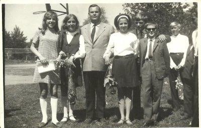 Fotografia przedstawia pozujących uczniów Szkoły Podstawowej w Lęborku wraz z nauczycielem. Wszyscy ubrani na galowo kilkoro uczniów trzyma kwiaty.  Rok: 1969