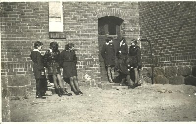 Fotografia przedstawia siedem uczennic przed wejściem do budynku Szkoły Podstawowej w Nowej Wsi Lęborskiej. Rok: 1968